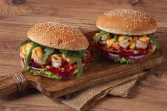 Two shrimp burgers and buns with sesame seeds, bacon, lettuce, tomatoes and onions, on a wooden