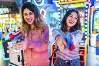 Two young women enjoying their free time playing together in an amusement arcade, holding toy guns