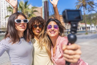 Three cheerful women taking a selfie with action camera, waving and smiling, enjoying a summer day