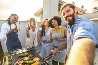 Cheerful friends enjoying rooftop barbecue party, grilling food and beverages and taking a selfie