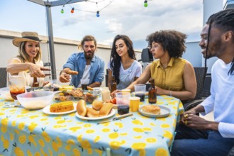 Cheerful friends sharing a meal together at a rooftop barbecue, enjoying grilled food, drinks, and