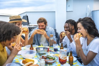 Cheerful multi ethnic friends savoring delicious burgers while enjoying a lively rooftop barbecue