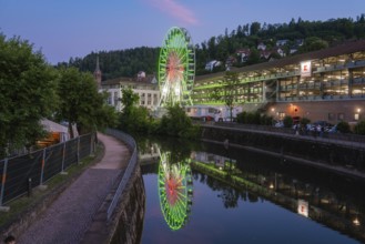 A Ferris wheel shines in blue and green and is reflected in a calm river at night, 950 years of
