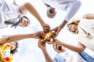 Group of cheerful multi ethnic friends toasting with beer bottles, enjoying a summer beach party