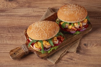 Two shrimp burgers and buns with sesame seeds, bacon, lettuce, tomatoes and onions, on a wooden