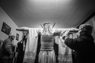 A man is tied to a cross with hemp ropes, he carries two swords in his back, a shroud over them, on