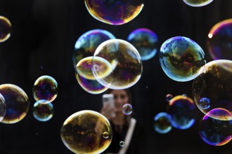 A woman photographs shimmering and floating soap bubbles against a black background,