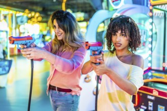Two women laughing and enjoying their free time while playing colorful arcade shooting games,