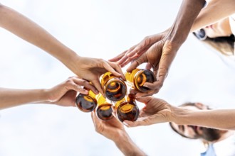 Group of friends toasting with beer bottles against a bright sky, celebrating friendship and