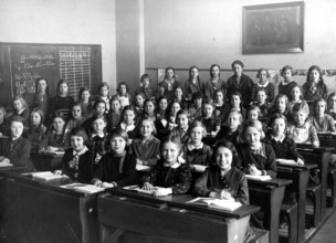Girls' class school bench, 1920s, A group of schoolgirls sitting on wooden benches in a classroom,