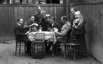 Round of cards, men playing cards, 1910, Group of people sitting outside at a table playing cards.