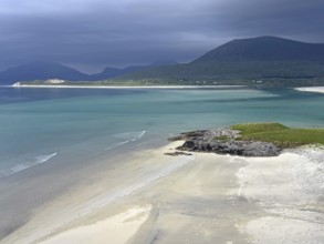 Dramatic sky over a calm beach with turquoise water and mountains in the background, Outer