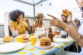 Happy friends enjoying burgers and beer, celebrating togetherness on a rooftop with string lights