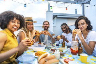 Cheerful multi ethnic friends savoring delicious burgers while enjoying a vibrant rooftop barbecue