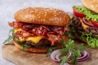 Two burgers with beef patty, fried bacon, cheddar cheese, tomatoes, homemade, no people