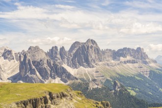 Imposing mountain range with dramatic sky and clouds, green plains below, hike to the Schlehrn,