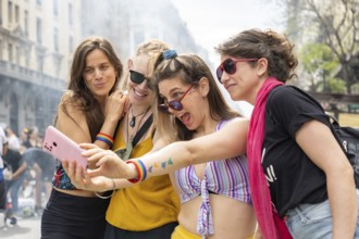Four young women wearing rainbow bracelets are taking a selfie with a smartphone during a gay pride