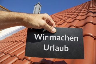 Roofer on holiday: Man holding a sign (with added text) WIR MACHEN URLAUB in front of a new tiled