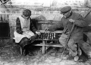 Old man playing chess with girl 1900, Two elderly people playing chess on a bench outdoors,