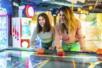 Two young women enjoying a friendly game of air hockey in a vibrant arcade, showcasing fun and