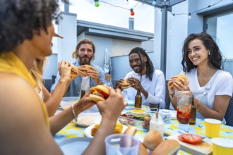 Cheerful multi ethnic friends savoring burgers and drinks while enjoying a lively rooftop barbecue