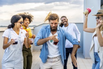 Young people enjoying drinks and dancing joyfully at a vibrant rooftop party, celebrating summer