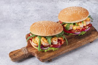 Two shrimp burgers and buns with sesame seeds, bacon, lettuce, tomatoes and onions, On a wooden