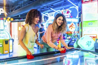 Two young women enjoying a friendly game of air hockey in a vibrant arcade, illuminated by colorful