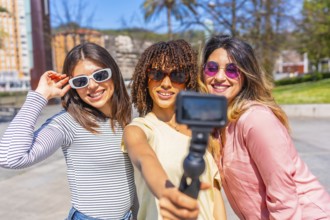 Multi ethnic women enjoying summer urban vacation, using action camera to film themselves,