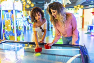 Two young women enjoying a friendly game of air hockey in a vibrant arcade, showcasing the fun and