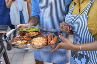 Chefs holding tray with sausages, burgers, chicken skewers and peppers, ready to serve at barbecue