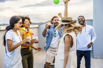 Cheerful multi ethnic friends enjoying cocktails while dancing joyfully at a vibrant rooftop party,