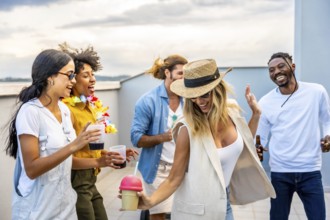 Cheerful multi ethnic friends enjoying cocktails and dancing joyfully at a vibrant rooftop party