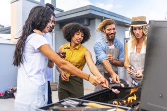 Cheerful friends roasting marshmallows on skewers over a barbecue grill during a rooftop party