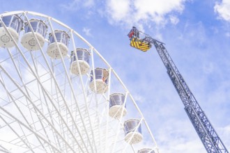 A crane near a Ferris wheel lifts equipment against a cloudy sky, fire brigade exercise for gondola