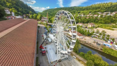 View of a Ferris wheel in a wooded environment with red roofs and blue sky, fire brigade exercise