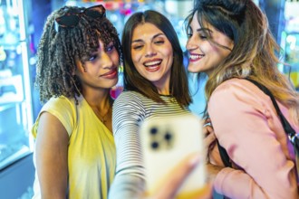 Three cheerful young women enjoying a fun moment together, taking a selfie with a smartphone in a
