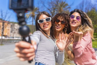 Three cheerful young women enjoying a summer day in the city, capturing a fun selfie with a gimbal,