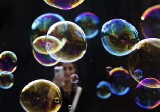 A woman photographs shimmering and floating soap bubbles against a black background,