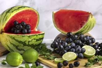 Sliced watermelon, grapes and limes on a wooden board with mint leaves