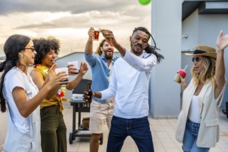 Cheerful friends toasting and dancing together at a vibrant rooftop party, enjoying drinks and