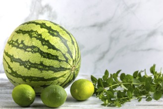 Watermelon and limes with mint leaves on a wooden surface