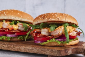 Two shrimp burgers and buns with sesame seeds, bacon, lettuce, tomatoes and onions, On a wooden