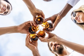 Group of diverse friends are holding and toasting glass bottles of beer together, celebrating under