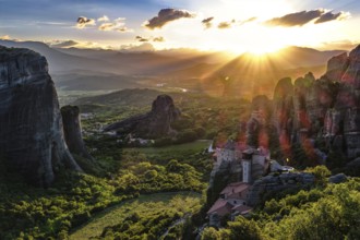 Iconic view of Meteora valley at sunset. Sun setting behind distant mountains, sun rays fall on