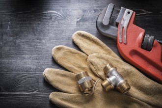 Pipe wrench plumbing fittings safety gloves on wooden board