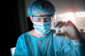 Surgeon in dim light holding a syringe, focused and wearing protection