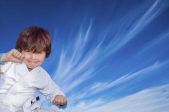 Handsome boy in a white kimono practices judo. Background - flying cirrus clouds and blue sky.