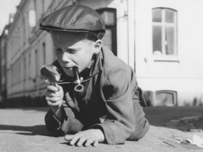 Playing detective. A young boy dressed as a typical looking detective with a magnifying glass and a