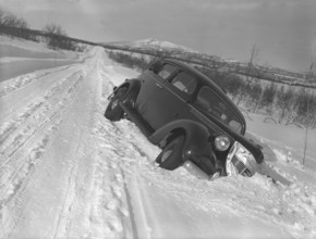 Winter driving in the 1930s. A car has skidded of the snowy road down and is stuck in the snow